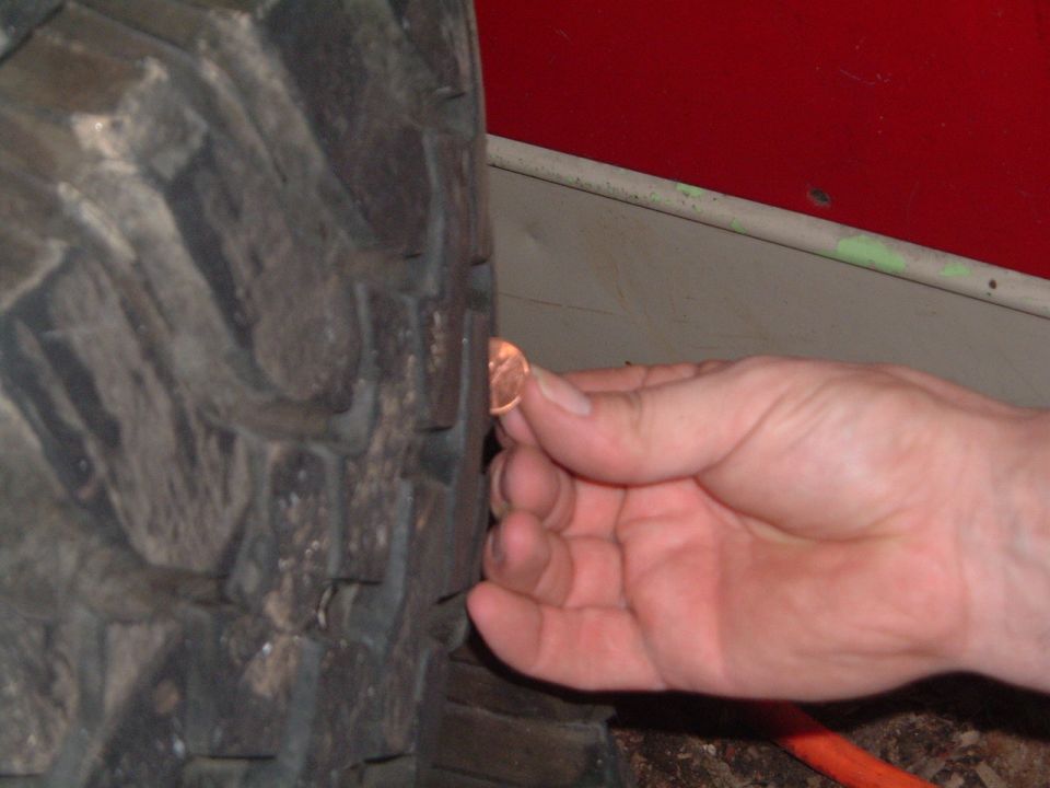 Hand holding a penny to measure tread depth on a tire