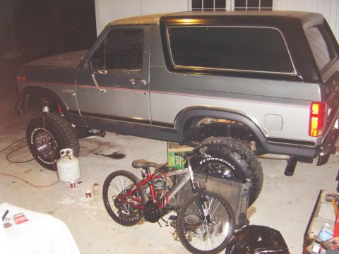 1986 Ford Bronco - This lifted two-tone SUV is parked indoors, surrounded by bicycles and equipment.
