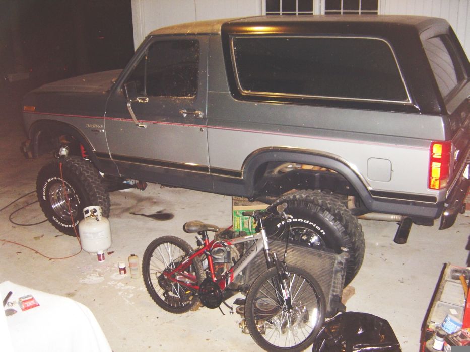 Lifted two-tone SUV with off-road tires, parked indoors with bicycles