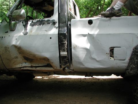 1977 Ford F-150 - This heavily damaged pickup truck shows extensive dents and wear along its side panels, with mud splattered on the lower panels.