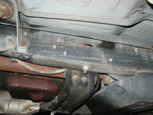 1989 Ford Bronco - Close-up view of the underside of a vehicle's frame, showing structural components and the transmission pan. The Supermotors.net logo is pr…