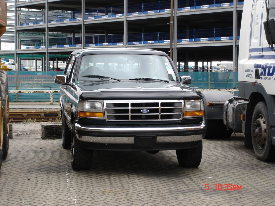Black Ford pickup truck, front view with chrome grille, parked near a semi cab and steel construction site