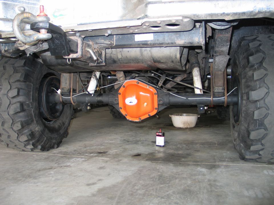Underside of lifted truck showing solid rear axle with orange-painted differential cover and large mud tires