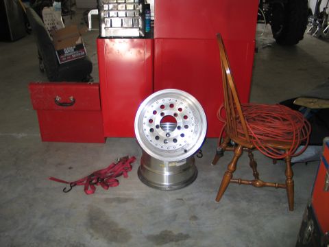 1992 Ford Bronco - An aluminum wheel is displayed in a garage setting, next to a wooden chair with coiled red cord.