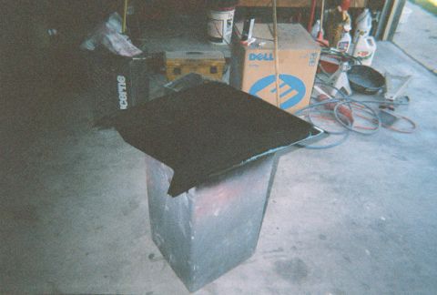 1972 Ford Ranchero - A dark object covered in black carpet rests on a grey stand, surrounded by garage clutter.