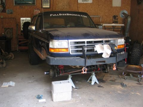 1995 Ford Bronco - 1995 Ford Bronco undergoing front-end work in a garage, with suspension components visible.