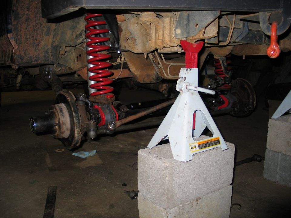 Front suspension underside with red coil springs and rotor exposed, truck on jack stand and concrete block