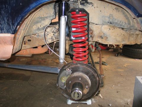 1995 Ford Bronco - Close-up of a vehicle's front suspension and brake system, showing a red coil spring and silver shock absorber.