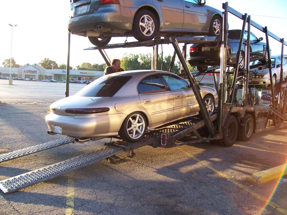 Gold Mercury Sable sedan being unloaded down the ramps of a car hauler trailer