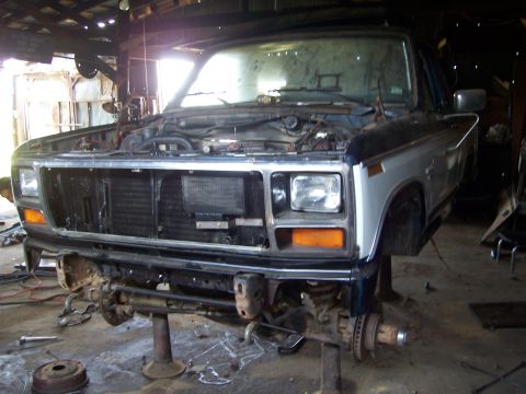 1983 Ford Bronco - This Ford truck is undergoing repairs in a garage, with its front end lifted and parts removed.