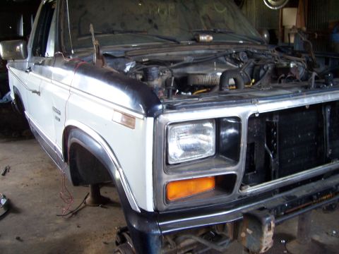 1983 Ford Bronco - This Ford Bronco is undergoing repairs in a garage, with its hood up and front end exposed.