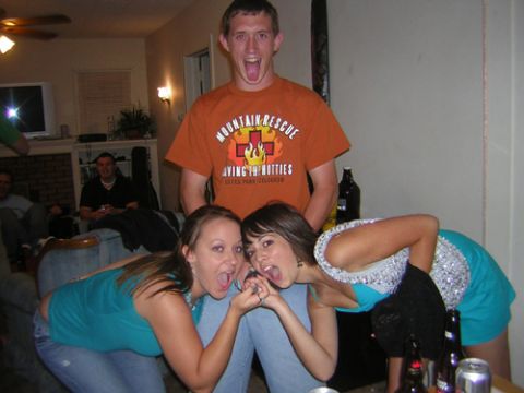 1995 Ford Bronco - Three people posing and making exaggerated faces at an indoor party; a tall man in an orange 'Mountain Rescue' t-shirt stands behind two wo…