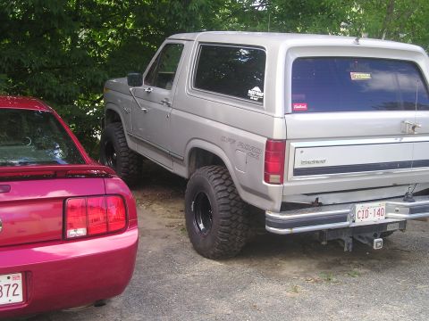 1984 Ford Bronco - A silver Ford Bronco with off-road tires is parked next to a red vehicle.