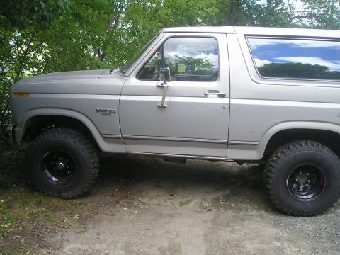 1984 Ford Bronco - Side profile of a silver 1984 Ford Bronco, its distinctive body style and off-road tires.