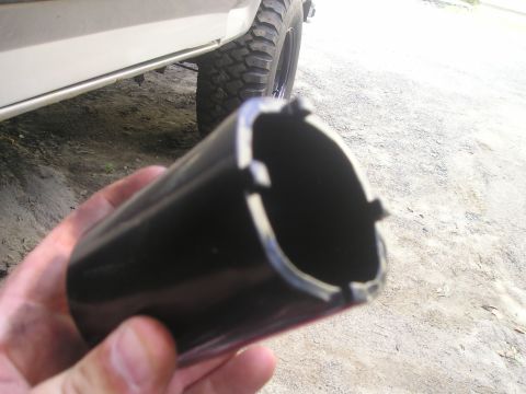 1984 Ford Bronco - A black tool part is held in front of a vehicle's tire and body.