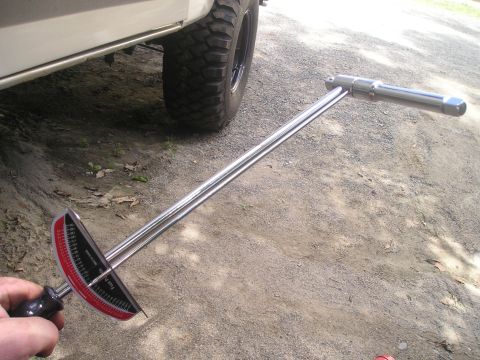 1984 Ford Bronco - A torque wrench is held near the wheel of a white vehicle with large off-road tires.
