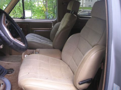 1984 Ford Bronco - The interior of the vehicle features cloth seats and a center console with a cup holder.