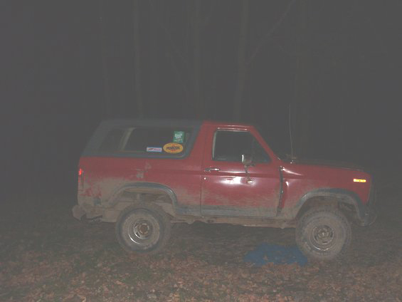 Red lifted Ford Bronco SUV, right side view, parked at night in the woods