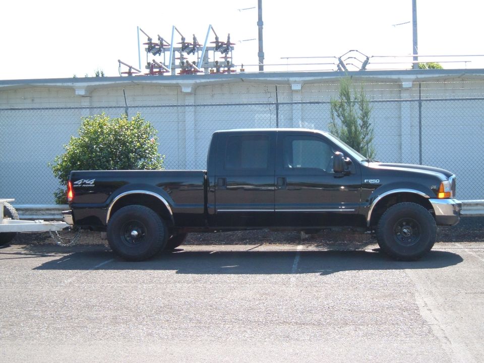 Black Ford F-250 crew cab pickup, side view, parked in a lot near a substation.