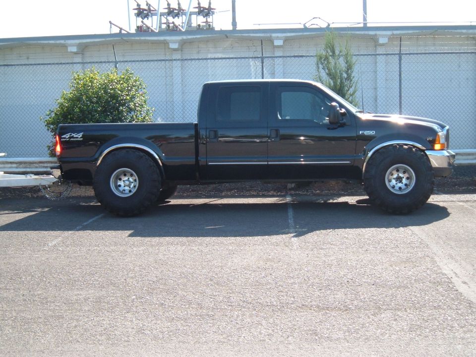 Black Ford F-250 crew cab 4x4 pickup with large off-road tires, side view in a parking lot