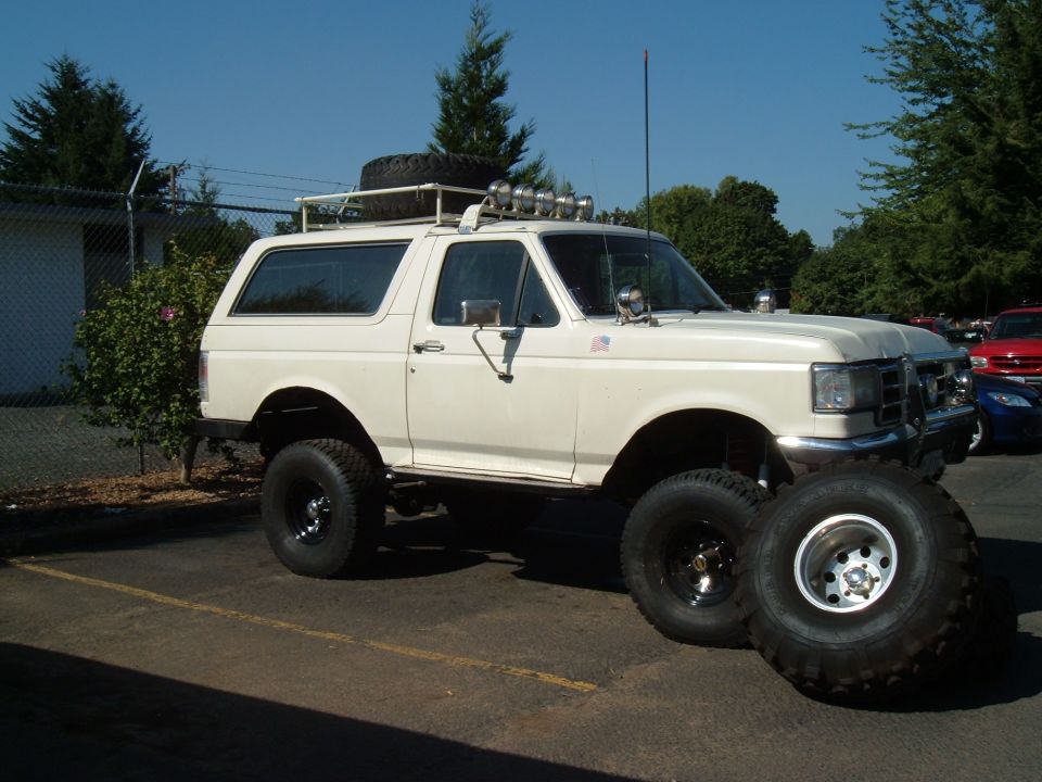 Lifted white Ford Bronco with roof rack, spare tire and off-road lights, spare tire leaning on front wheel