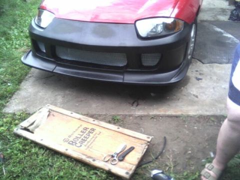 2005 Chevrolet Cavalier - Front view of a red car with a custom bumper and a roller creeper on the ground.