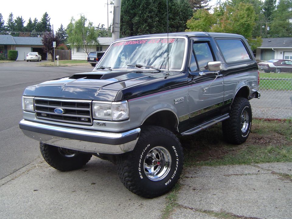 Lifted black and gray Ford Bronco on mud-terrain tires parked in a driveway, front 3/4 view