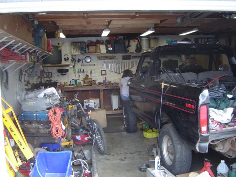 1989 Ford Bronco - A black 1989 Ford Bronco is parked inside a garage filled with tools and automotive parts.
