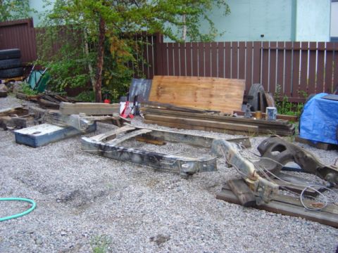 1986 Ford F-150 - Various vehicle chassis components are laid out on a gravel surface, with lumber and other materials nearby.