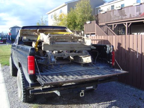 1986 Ford F-150 - A black pickup truck is viewed from the rear, with its tailgate down, loaded with a heavy metal assembly.
