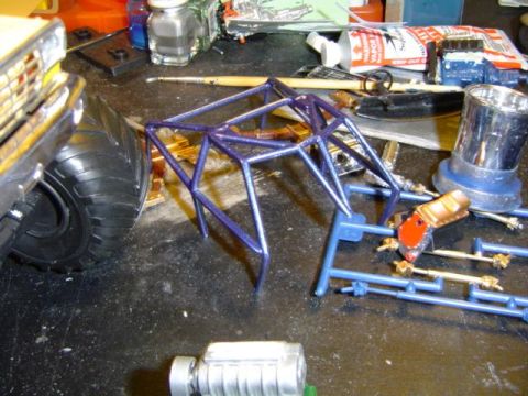 1979 Ford Bronco - Various components of a model vehicle are assembled on a cluttered workbench, suggesting a hobbyist's project.