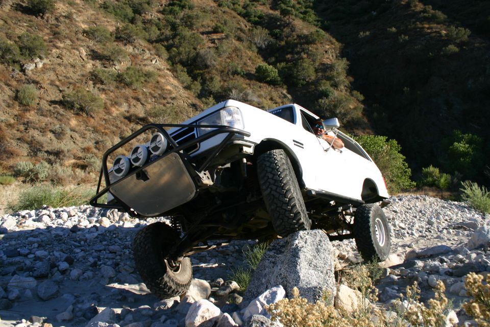 White lifted 4x4 SUV with brush guard articulating over rocks on a hillside trail