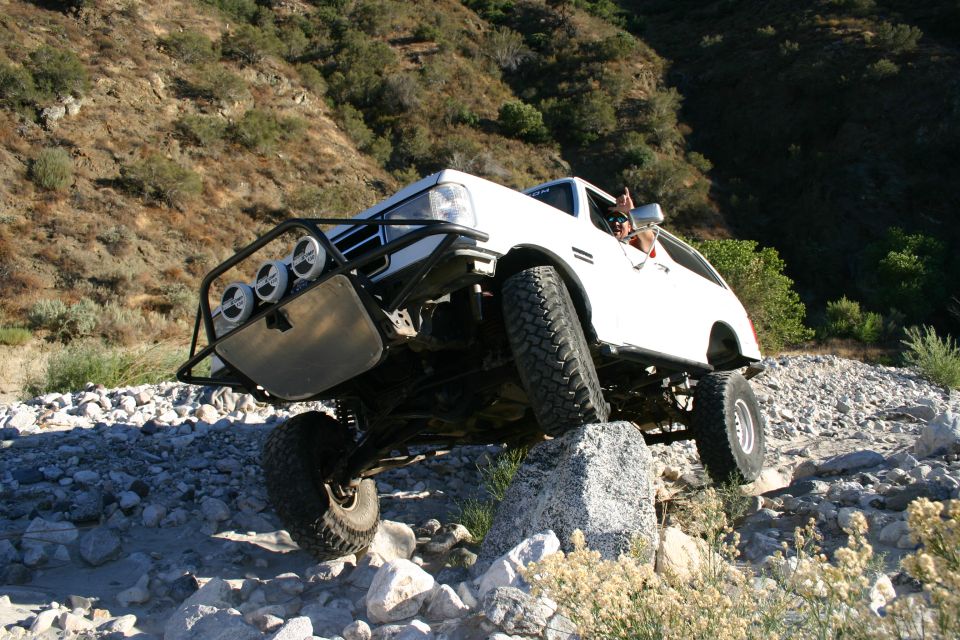 White lifted SUV with three driving lights cresting rocks in a brushy canyon