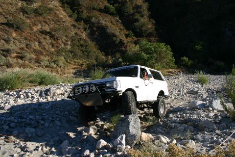 1990 Ford Bronco - white lifted SUV equipped with a brush guard and three driving lights works over scattered boulders in a steep rocky canyon.