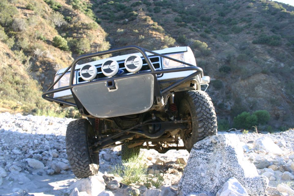 Low front angle of lifted SUV with brush guard and three lights flexing on rocks