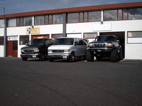 1996 Ford Bronco - Three vehicles, including a modified Ford Bronco, are parked outside a commercial building.