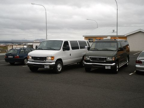 1996 Ford Bronco - Two Ford E-Series vans are parked in a lot, with a station wagon visible on the left.