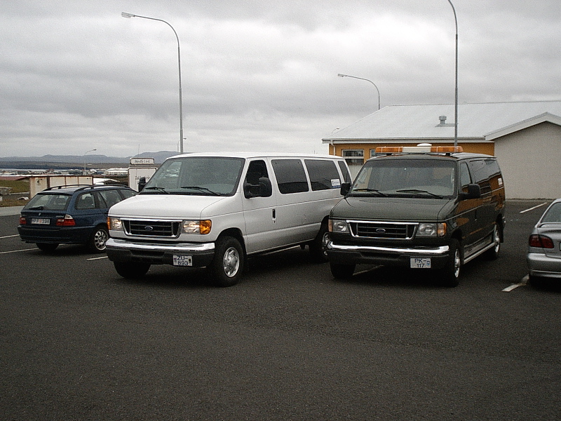 Silver and dark Ford Econoline vans parked in a lot under gray sky