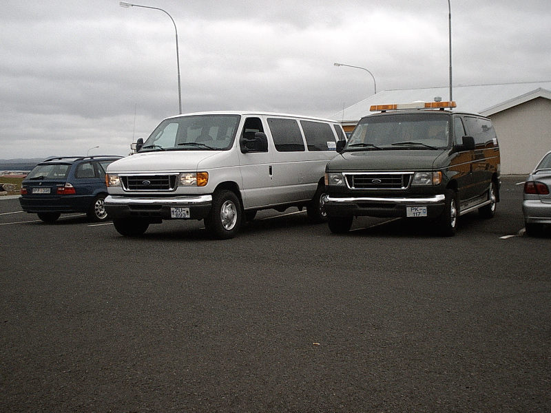 Silver and green Ford E-Series vans parked in a lot under gray skies
