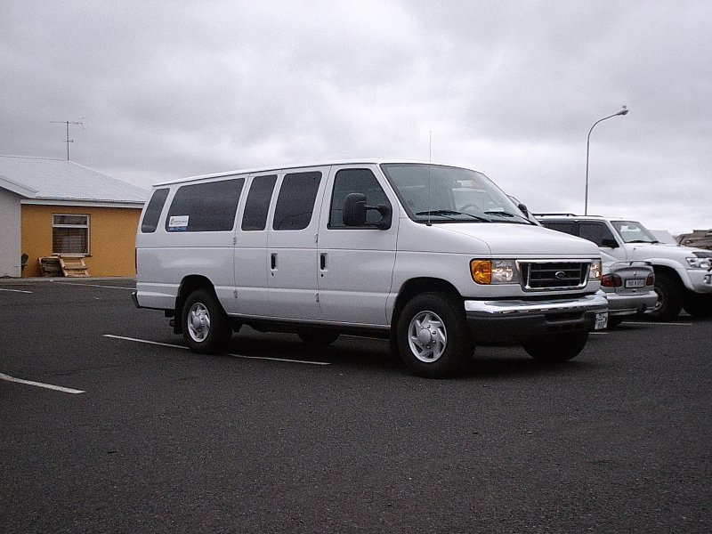 White Ford full-size passenger van parked in lot, front 3/4 view