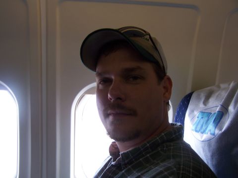 1979 Ford F-150 - A man with a mustache and baseball cap is seated inside an airplane cabin.