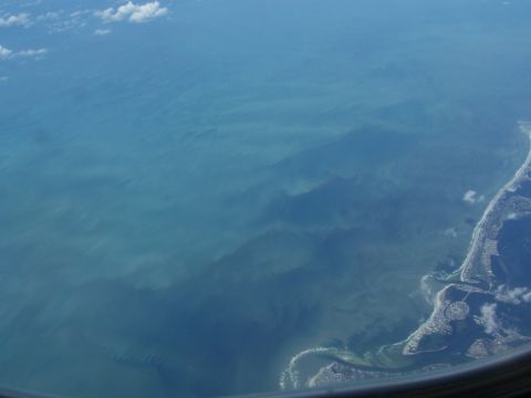 1979 Ford F-150 - View from an airplane window showing the ocean meeting the coast with scattered clouds.