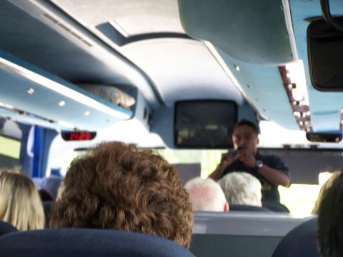 1979 Ford F-150 - Passengers inside a bus observe the driver who is speaking into a microphone. A digital clock displays 14:23.