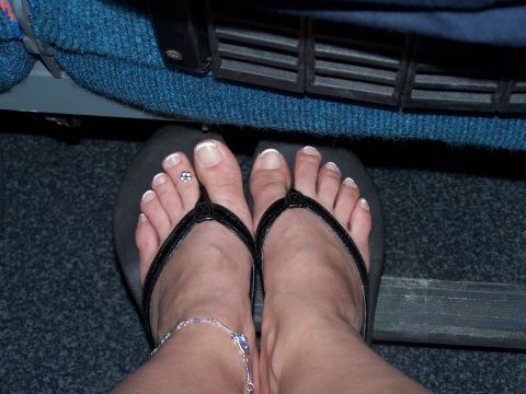 1979 Ford F-150 - A close-up view of feet wearing flip-flops and an anklet, resting near car pedals.