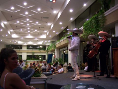 1979 Ford F-150 - A mariachi band performs on a stage in a brightly lit indoor venue, with an audience seated in the foreground.