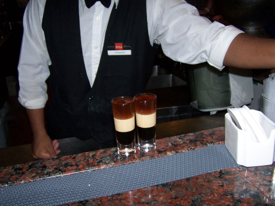 bartender in uniform with two layered shots on a granite bar top