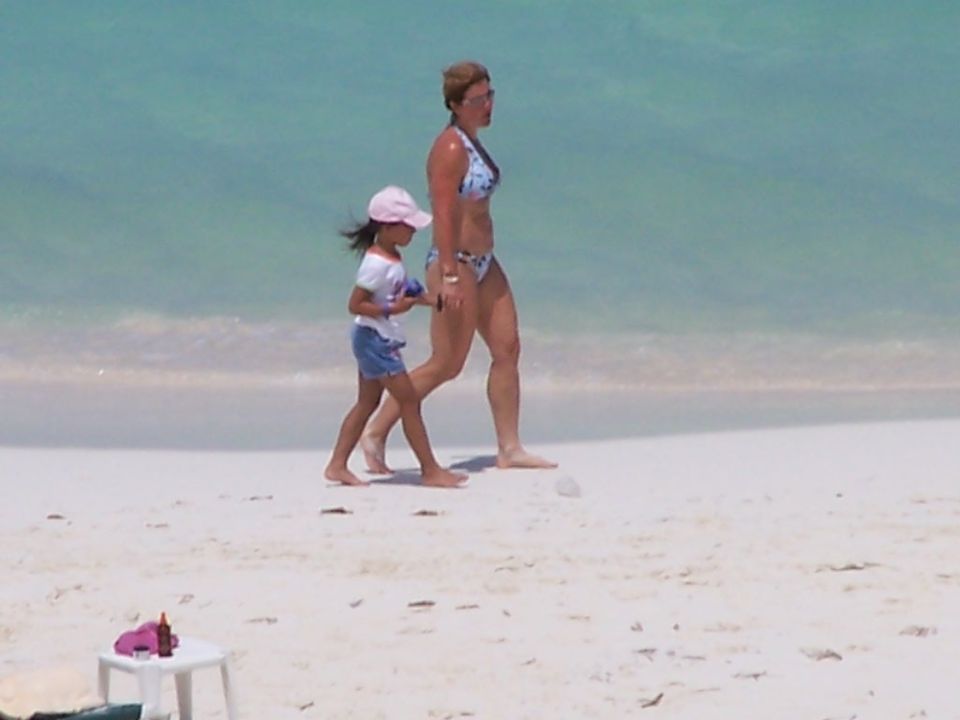 Woman and child walk on a sandy beach with turquoise water