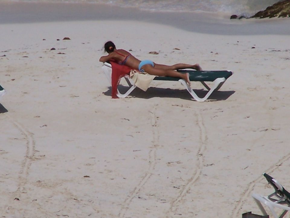 Woman in bikini lying on a lounge chair on a sandy beach with the ocean in the background