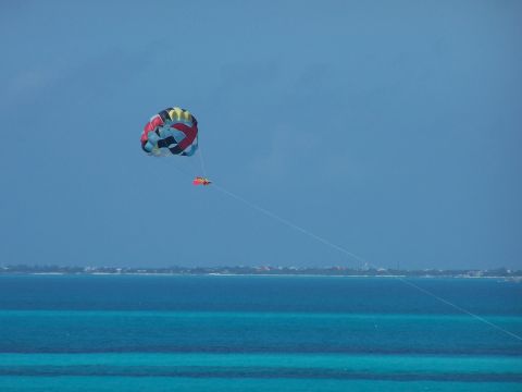 1979 Ford F-150 - A colorful parasail is towed by a boat over the turquoise waters of the ocean, with a coastline visible in the distance.