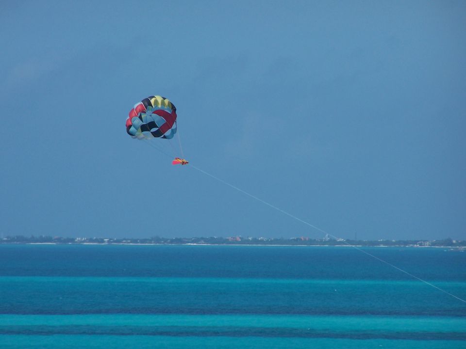 Parasailer high in the sky over bright blue ocean water with a distant shoreline